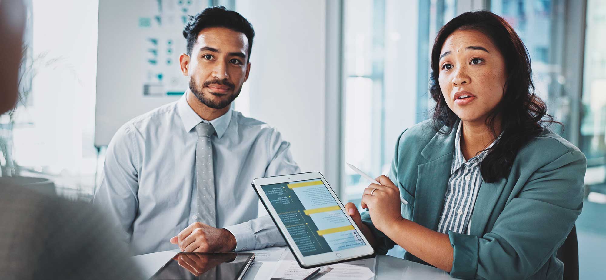 Dos profesionales discutiendo sobre un dispositivo móvil en un entorno de oficina, con documentos y gráficos de fondo.