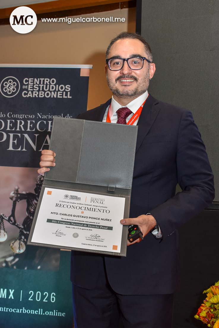 Hombre con gafas y traje sosteniendo un certificado de reconocimiento en un evento relacionado con derecho penal.