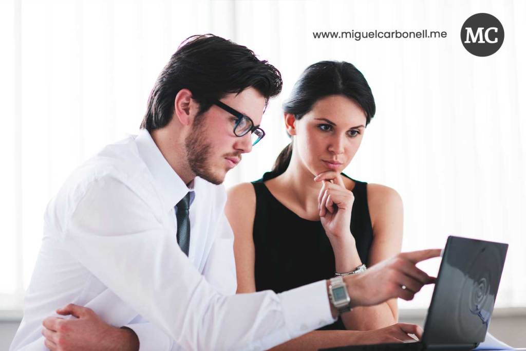 Un hombre y una mujer de negocios analizando información en una computadora portátil en un entorno de oficina.